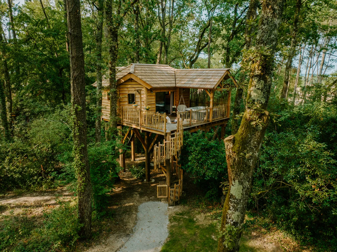 Elevated wooden treehouse cabin in a dense forest with wraparound deck and staircase access, in Bordeaux.