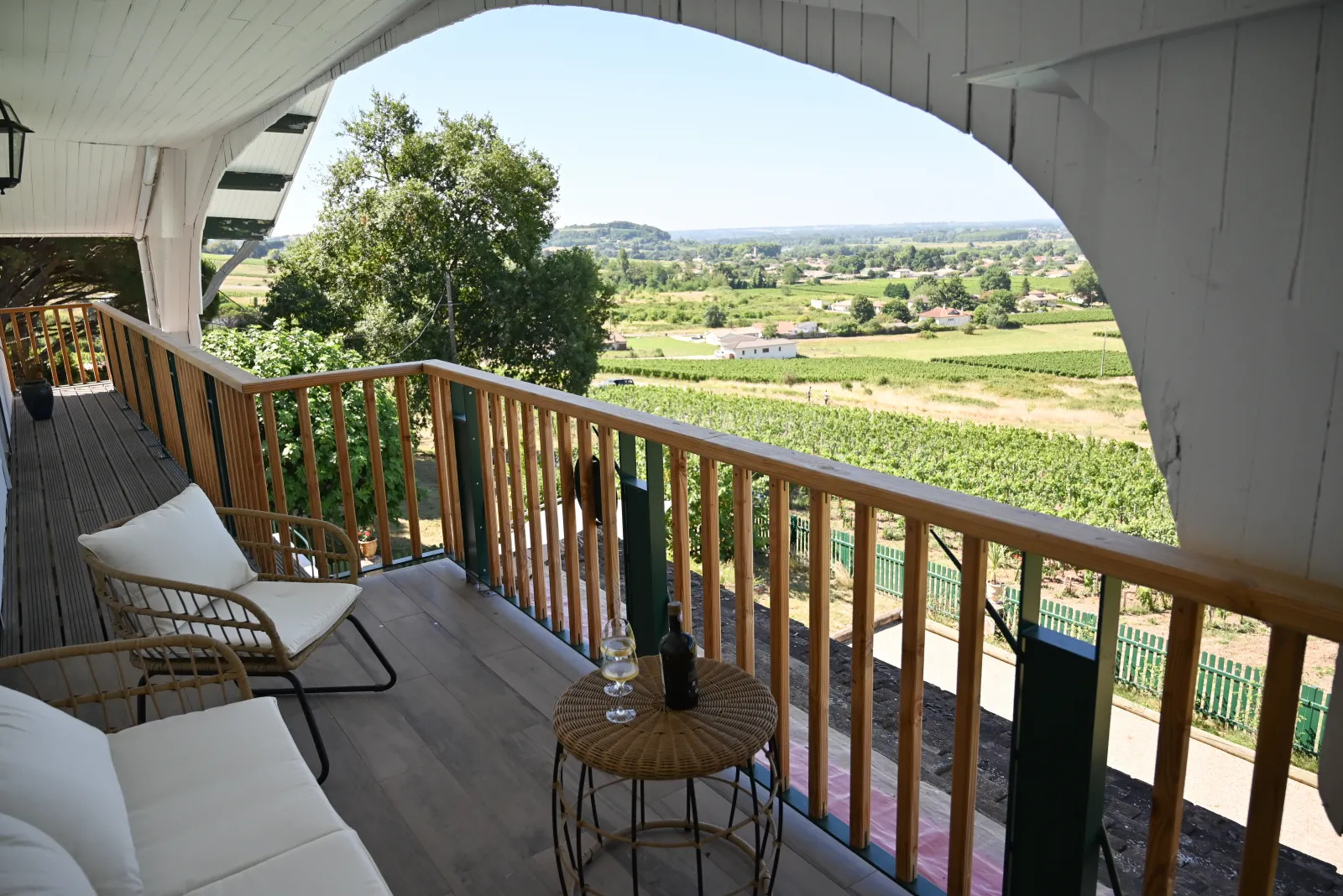 Covered terrace overlooking Bordeaux vineyards from Le Chalet des Perchés, featuring a lounge chair, round table, and expansive countryside landscape