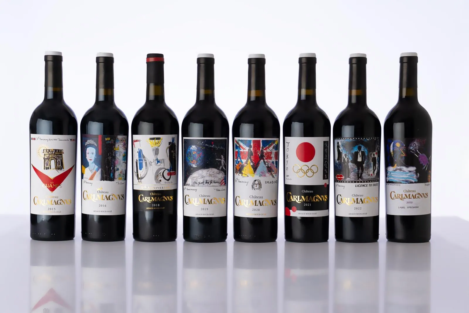 Set of eight red wine bottles from Château CarlMagnus in Bordeaux, vintages 2013 to 2022, displayed in a row with diverse artistic labels
