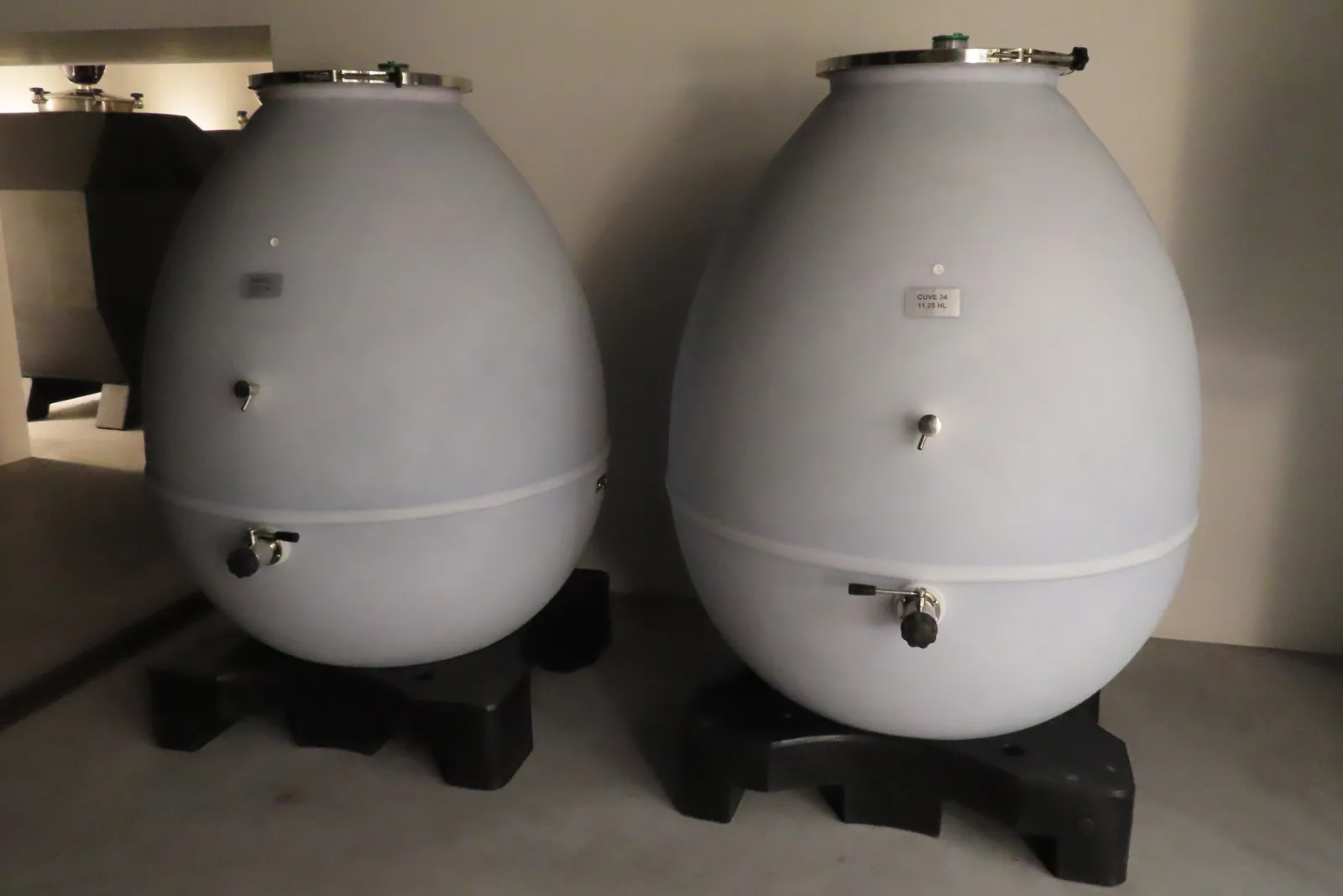 Two white spherical wine storage tanks with drain valves, mounted on black supports in the cellar of Château Pierre de Montignac in Bordeaux.