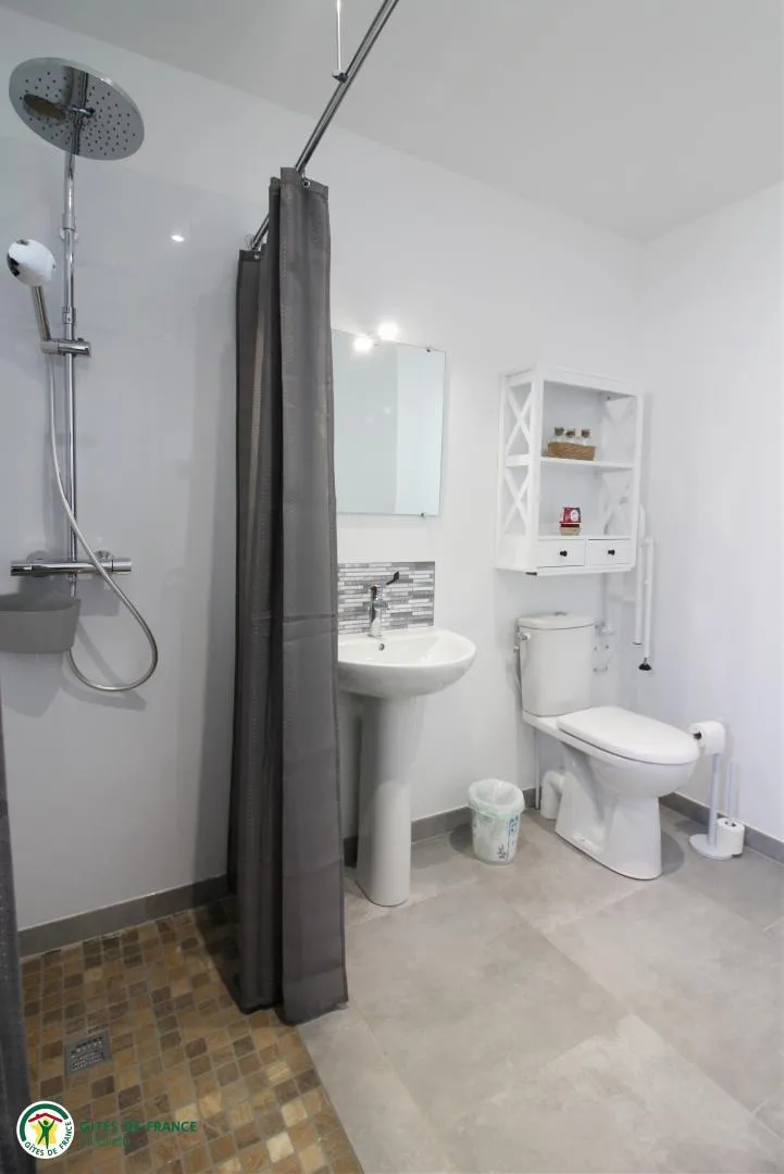 Modern bathroom of the Tanins gite at Château Pierre de Montignac in Bordeaux, featuring a walk-in shower, toilet, pedestal sink and white wall storage