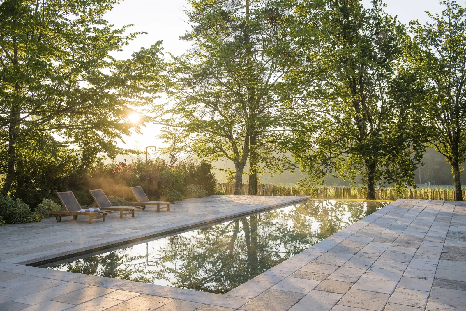 Terrace with reflection pool surrounded by trees, lounge chairs and wooden fence at La Chartreuse Haut-Bailly near Bordeaux