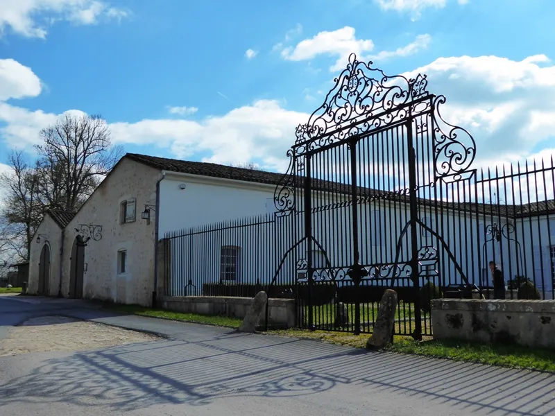 Château de Lisennes in Bordeaux featuring an ornate wrought iron gate, white façade, and impressive entrance portal against a clear blue sky.