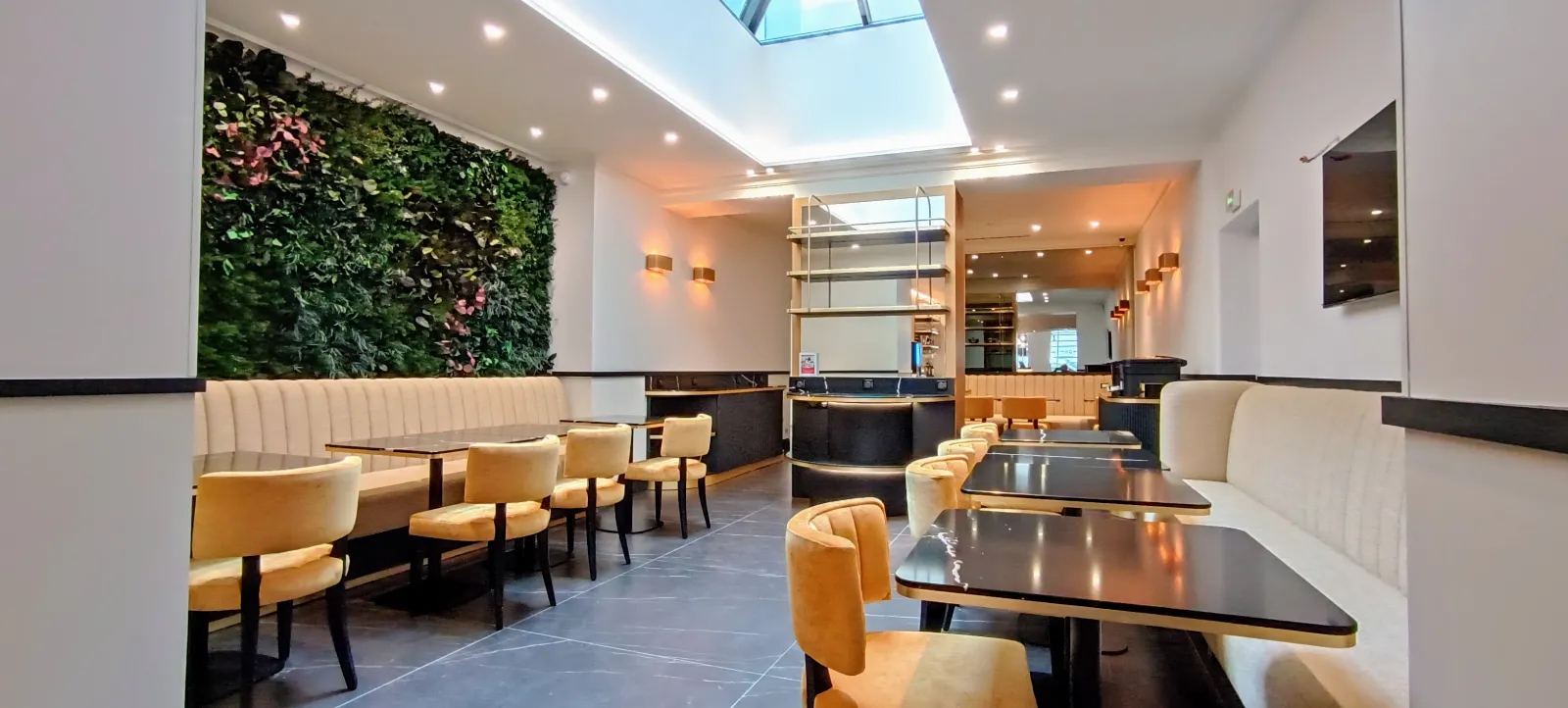 Modern lounge of Hotel Majestic in Bordeaux featuring beige leather seating, black coffee tables, living green wall with pink flowers, reception desk, mirrors and skylight ceiling