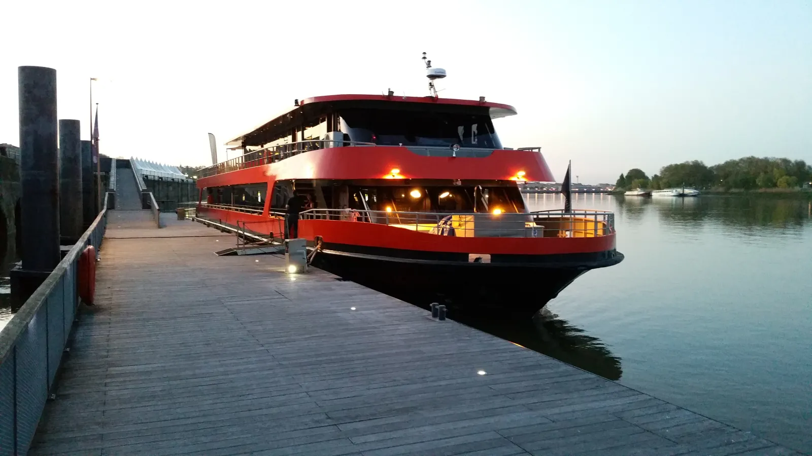 Red and black tourist boat moored at Bordeaux quay with lights on, ready for a cruise on the Garonne River.