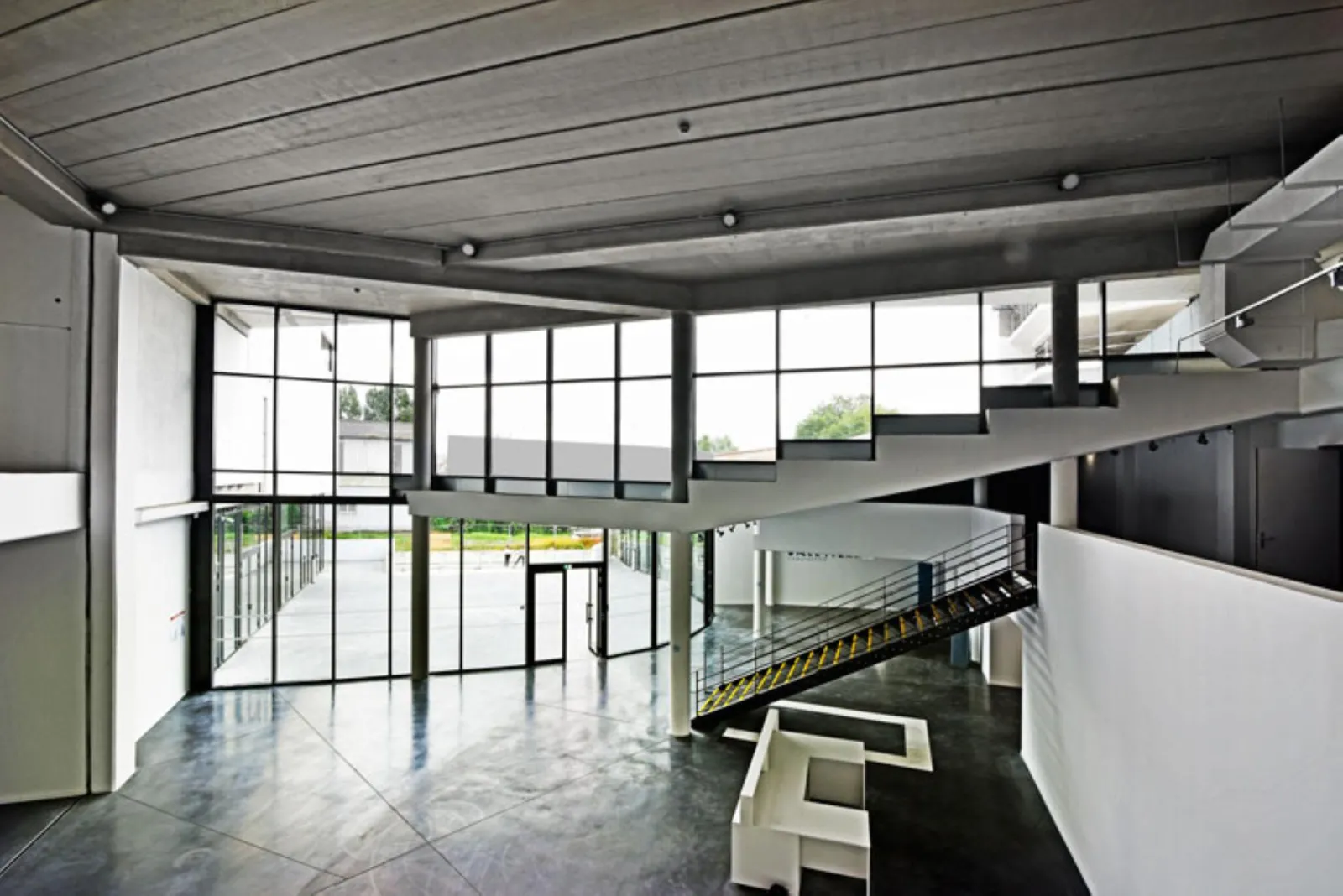Modern museum interior featuring metal stairs, expansive windows overlooking green landscape, exposed concrete ceiling and polished grey flooring at Bordeaux's Mer Marine Museum
