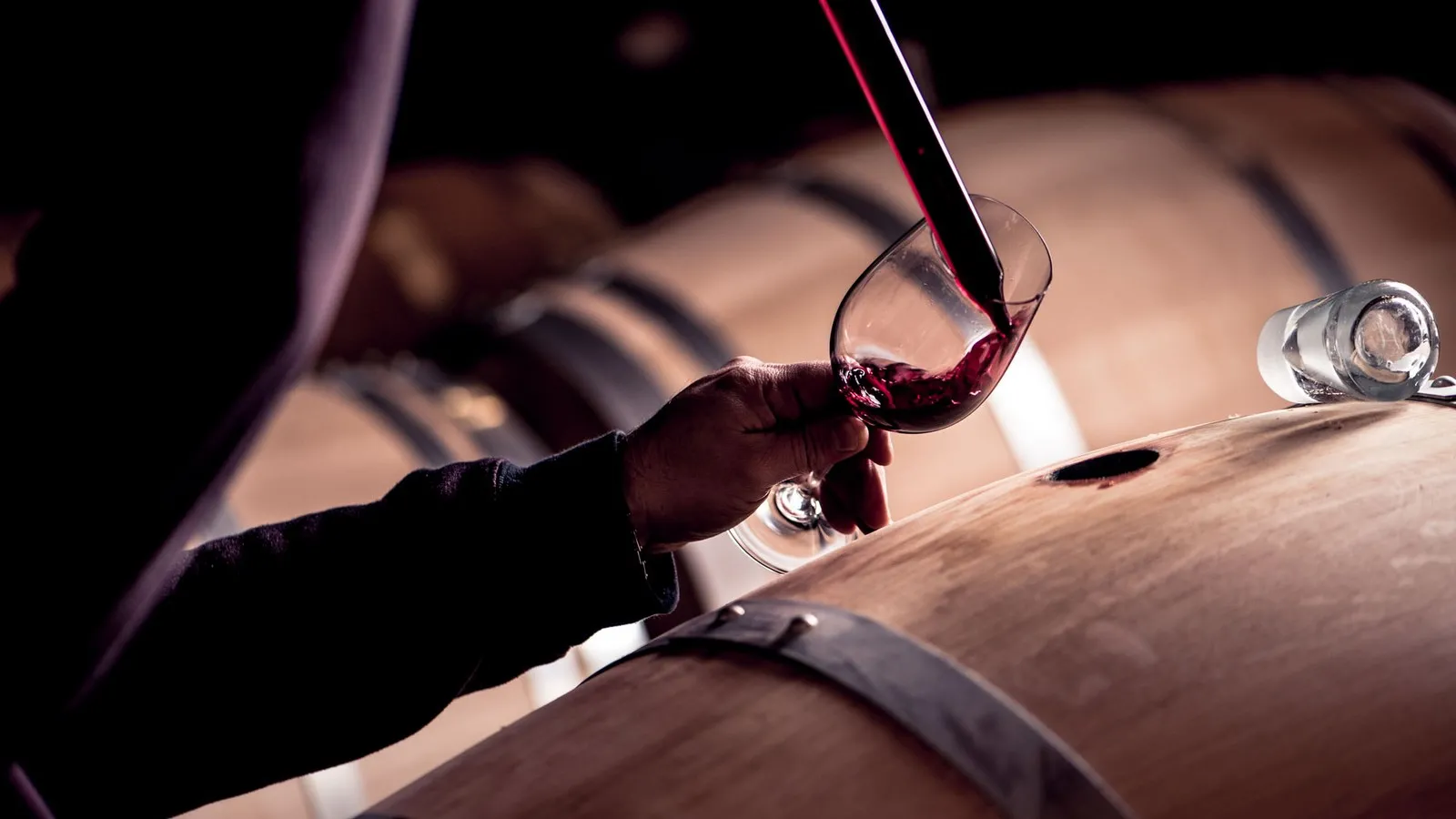 Red wine being poured into a glass during a tasting at Château d'Agassac in Bordeaux, with a decanter and glasses in the background