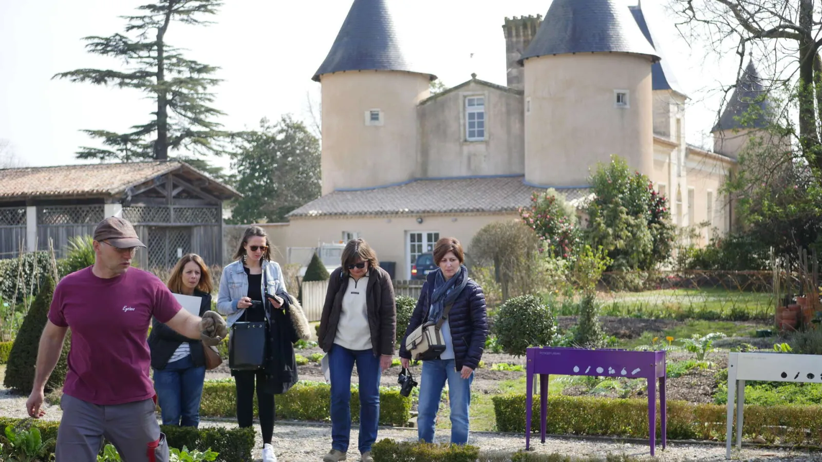 Guided tour at Bordeaux's Market Garden Museum with visitors walking through vegetable gardens in front of a castle with conical towers.