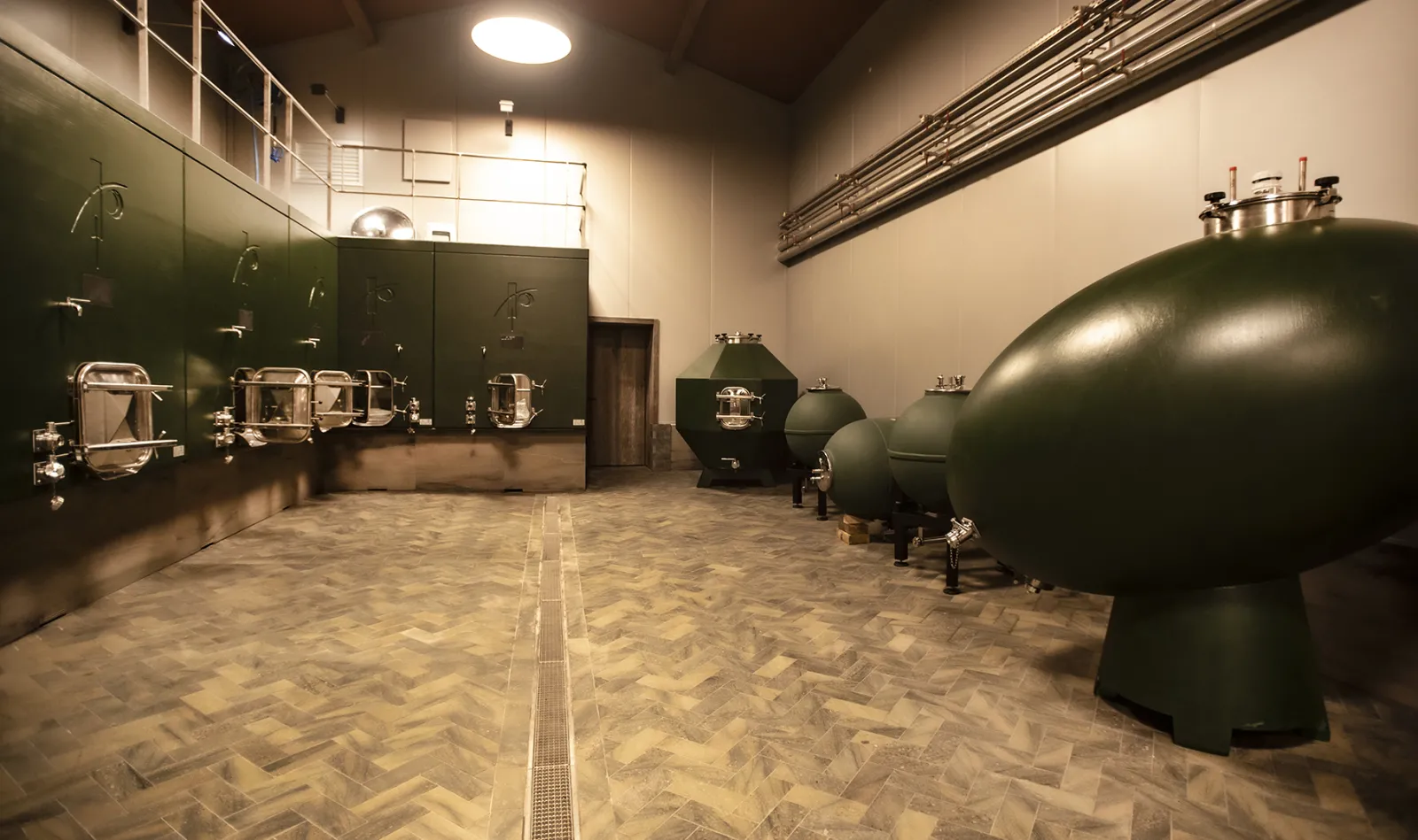 Winemaking facilities at Domaine des Perchés in Bordeaux: stainless steel fermentation tanks and concrete storage vats with modern cellar featuring dark walls and tiled flooring.