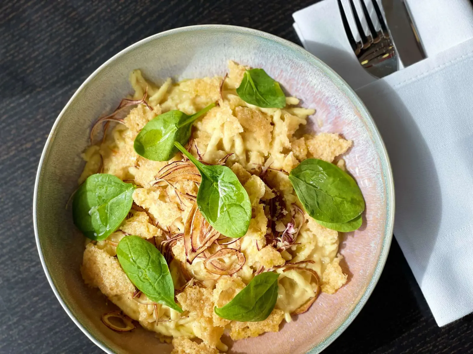Plate of creamy egg pasta topped with fresh arugula leaves and golden mustard sprouts, served at a Bordeaux restaurant.