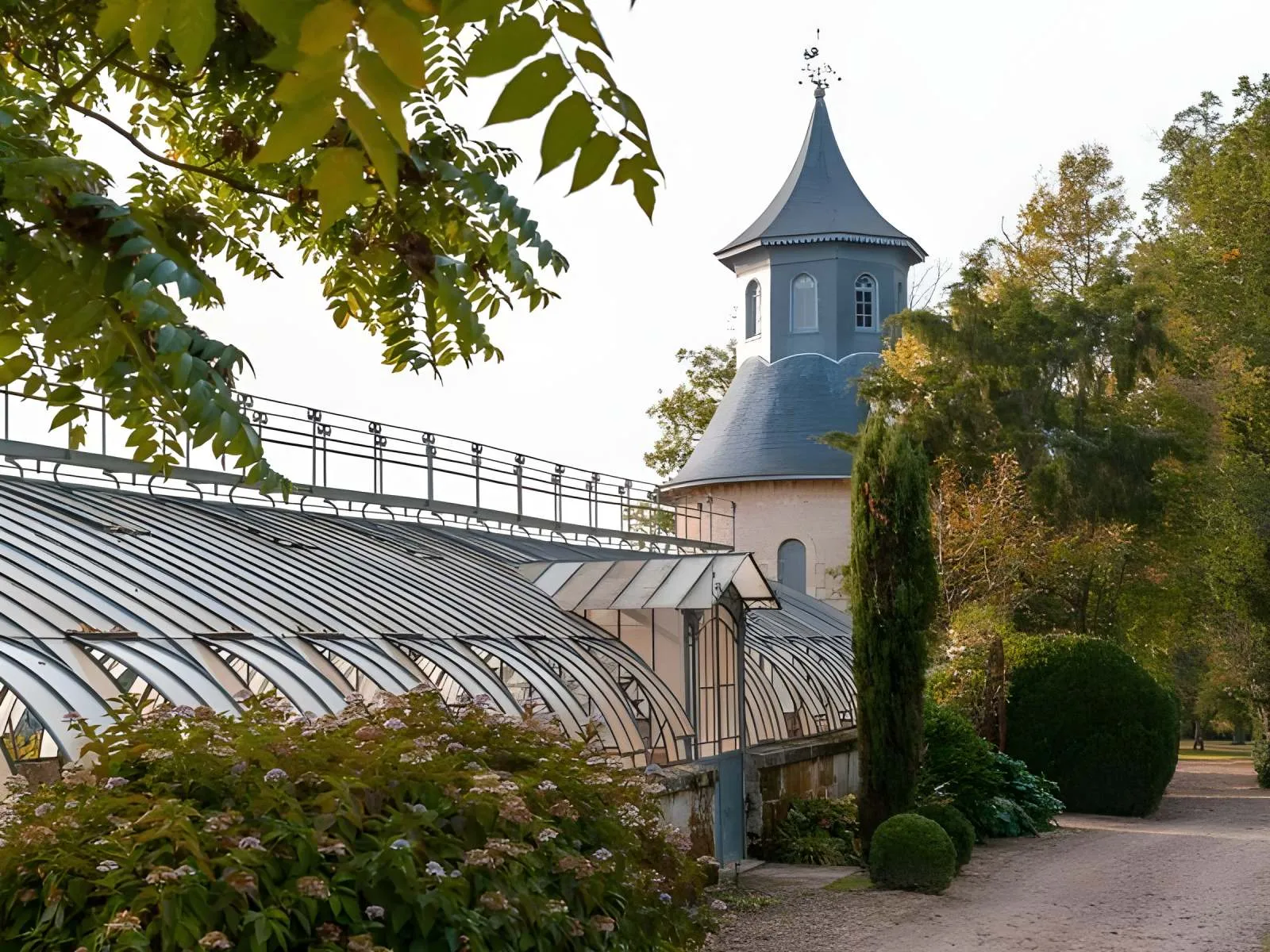 Château de Reignac in Bordeaux featuring a distinctive turret with slate-blue roof, a historic glass greenhouse, and manicured autumn gardens.