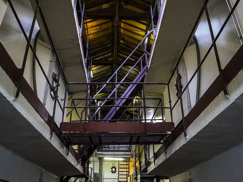 Interior view of a wine cellar with metal catwalks and multi-level storage structures illuminated by yellow and blue lighting.