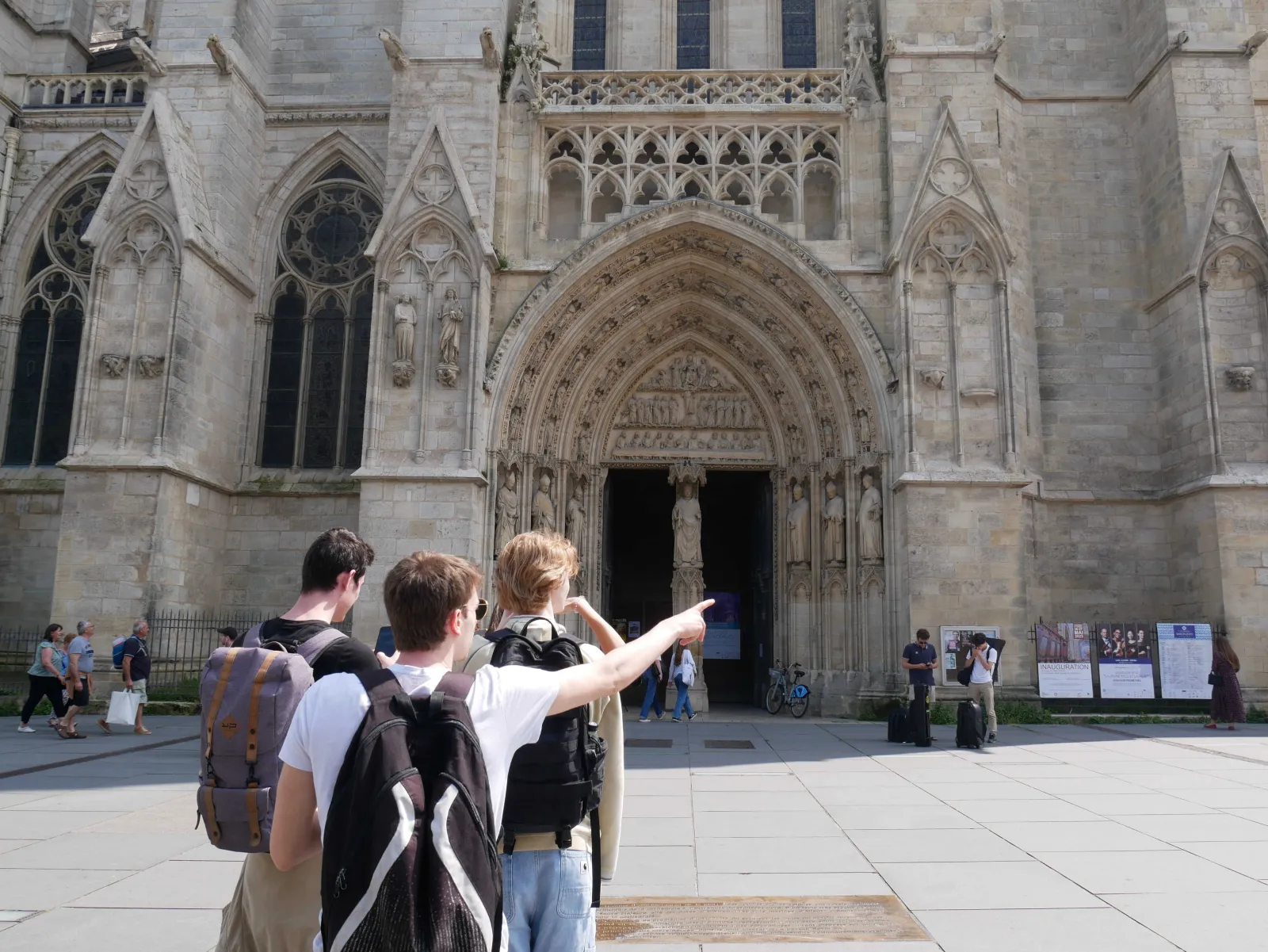 Three backpackers admiring the Gothic façade of Bordeaux Cathedral with its ornate portal, stained glass windows, and intricate stone carvings.