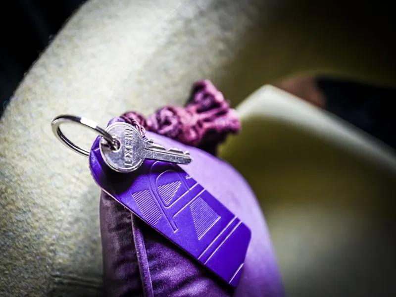 Silver key attached to a purple hotel key tag on white fabric