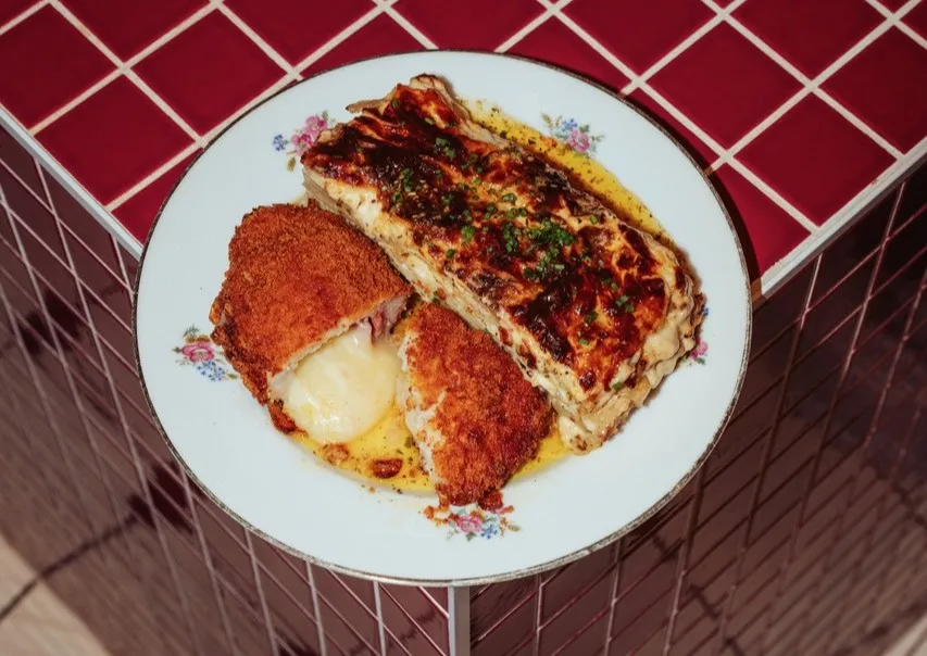 Roasted chicken thighs with crispy golden skin and a slice of topped bread served on a white floral-patterned plate at a Bordeaux rotisserie.