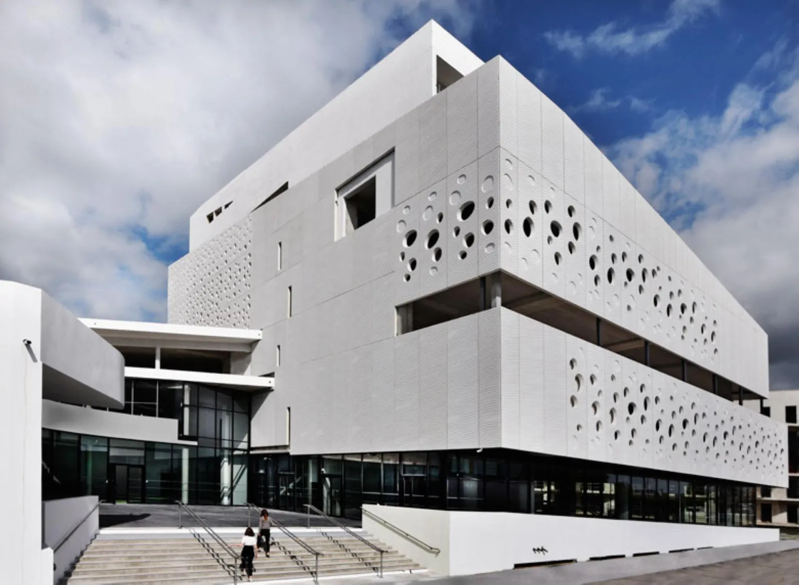Modern white façade of the Bordeaux Maritime Museum featuring circular perforations, access stairs, and blue sky backdrop