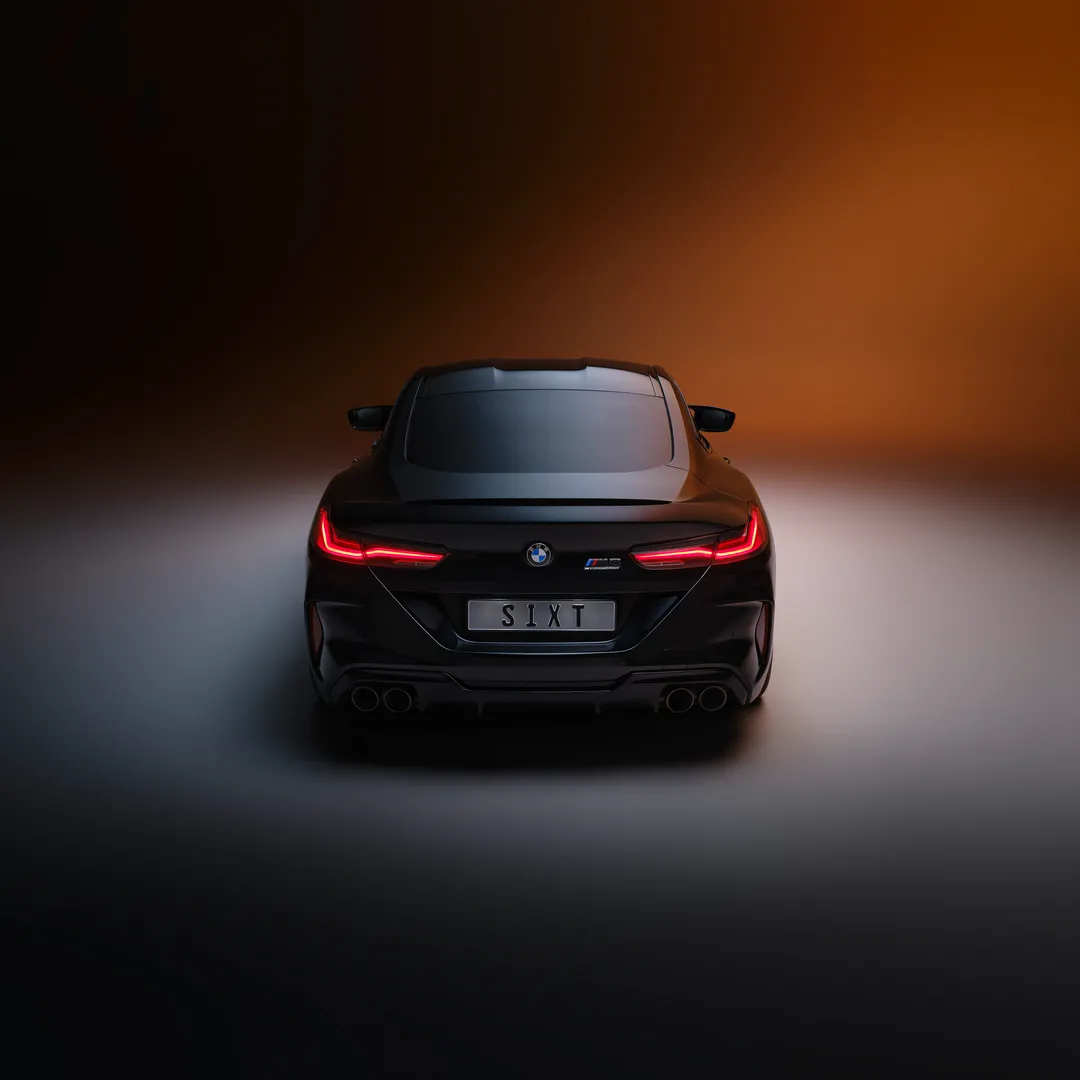Rear view of a black BMW M440i with illuminated red LED taillights and SIXT license plate, shot in studio with orange and gray gradient background