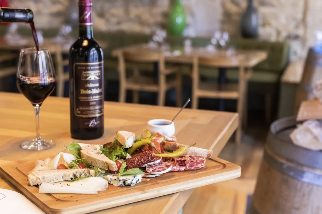 Charcuterie and cheese board served with a glass of red wine and a Bordeaux bottle on a wooden table in a restaurant