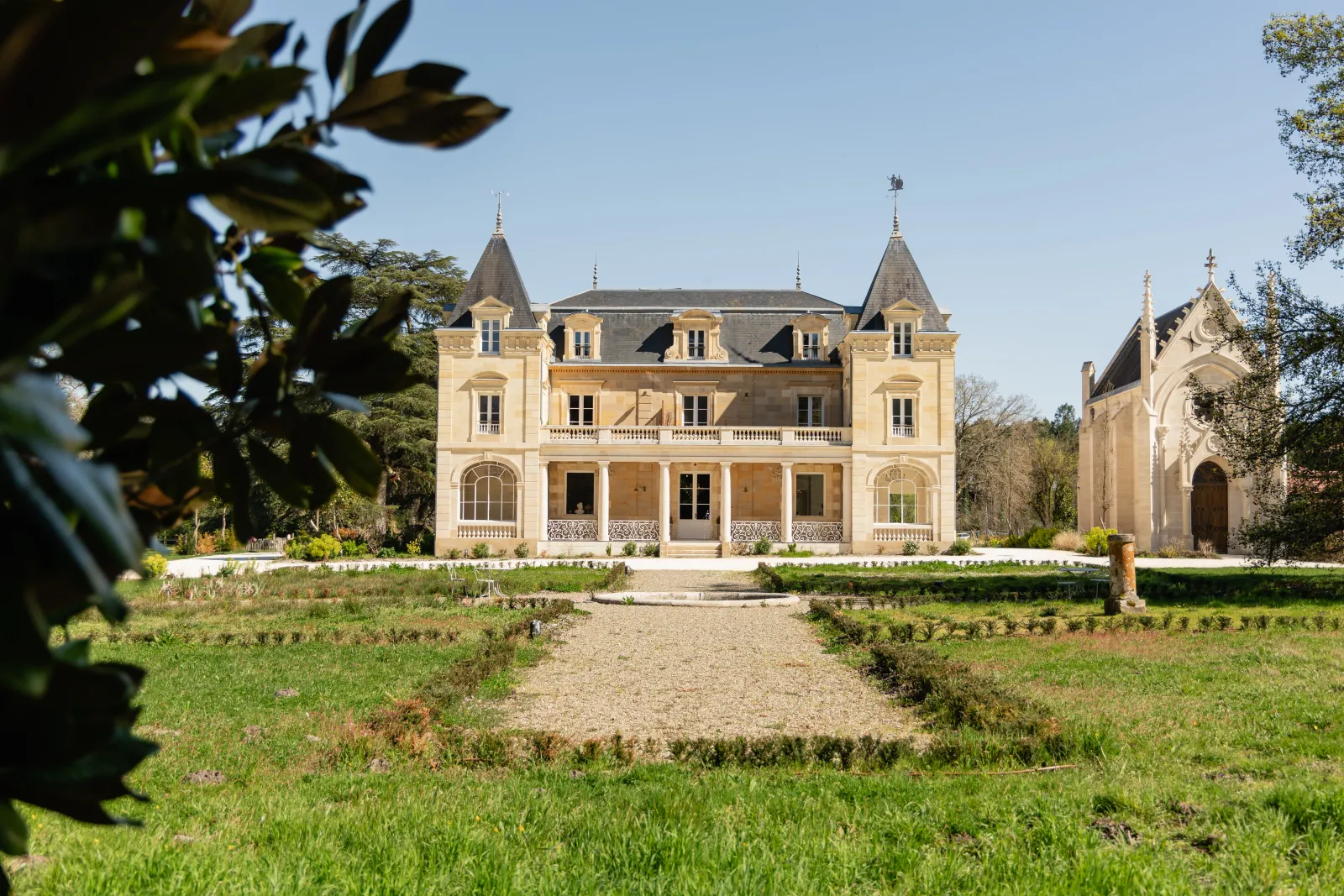 Château Léognan in Bordeaux, a grand Second Empire mansion with cream-colored facade, pointed turrets and slate roofs, surrounded by manicured gardens.