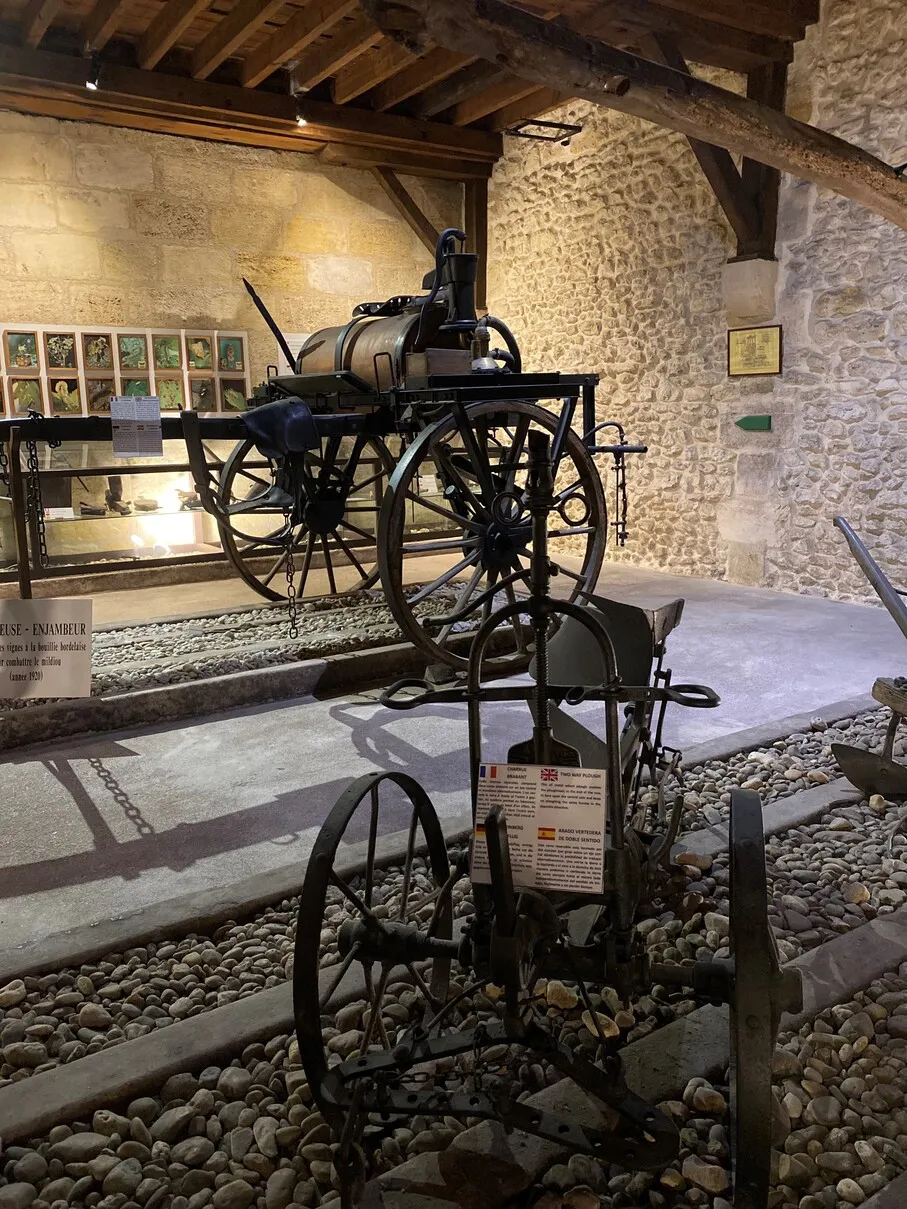 Historic steam plow on display in a vaulted cellar of Château Maucaillou in Bordeaux, with stone walls and historical exhibits in the background
