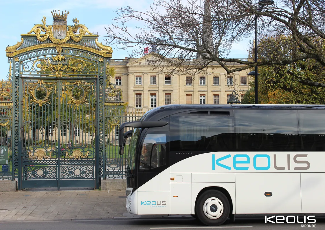 A white Keolis Gironde coach bus in front of the golden gates of the Élysée Palace in Bordeaux, with the neoclassical building visible in the background.