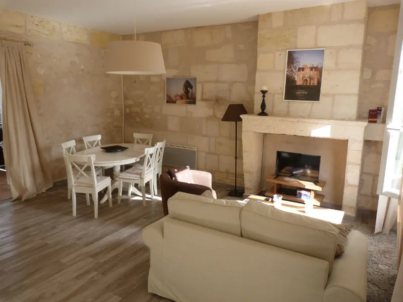 Elegant living room interior with fireplace, beige sofa, round white dining table, floor lamps and minimalist décor at Maison des Hôtesses in Bordeaux