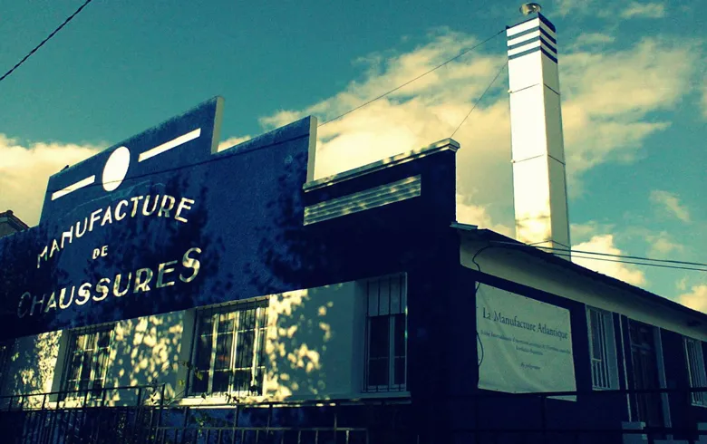 Bordeaux's La Manufacture industrial building featuring blue 'Shoe Manufacturing' sign and white chimney against a clear blue sky