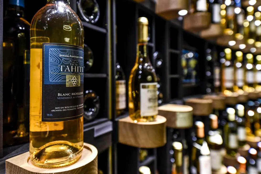 Bottle of Tahiti Blanc Moelleux white wine by Domaine Dominique Auvertin displayed at Latitude 20 Wine Bar in Bordeaux, surrounded by other wine bottles.