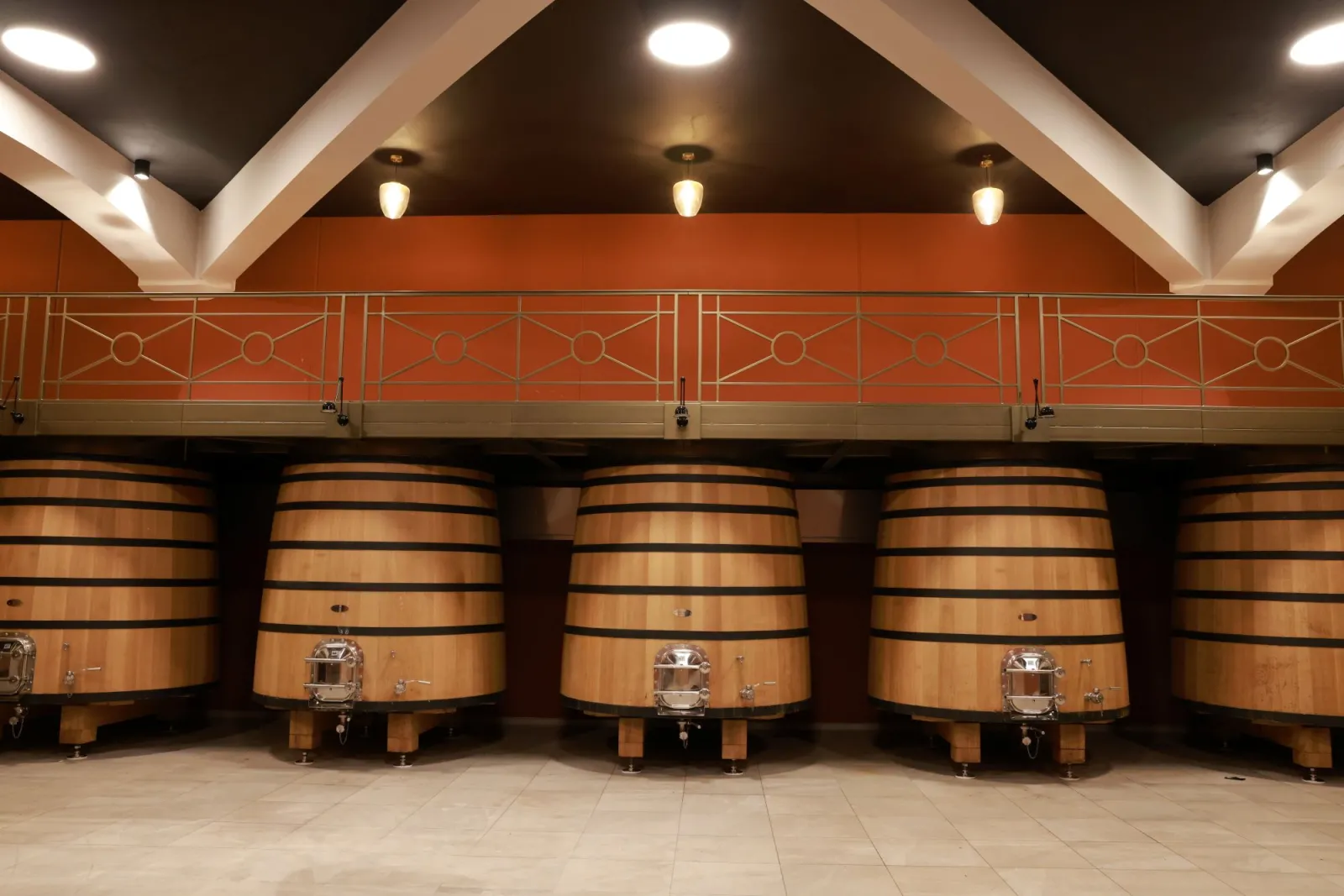 Aging cellar featuring rows of oak barrels under a vaulted ceiling with white beams, modern lighting and ochre walls, Château Plain Point in Bordeaux