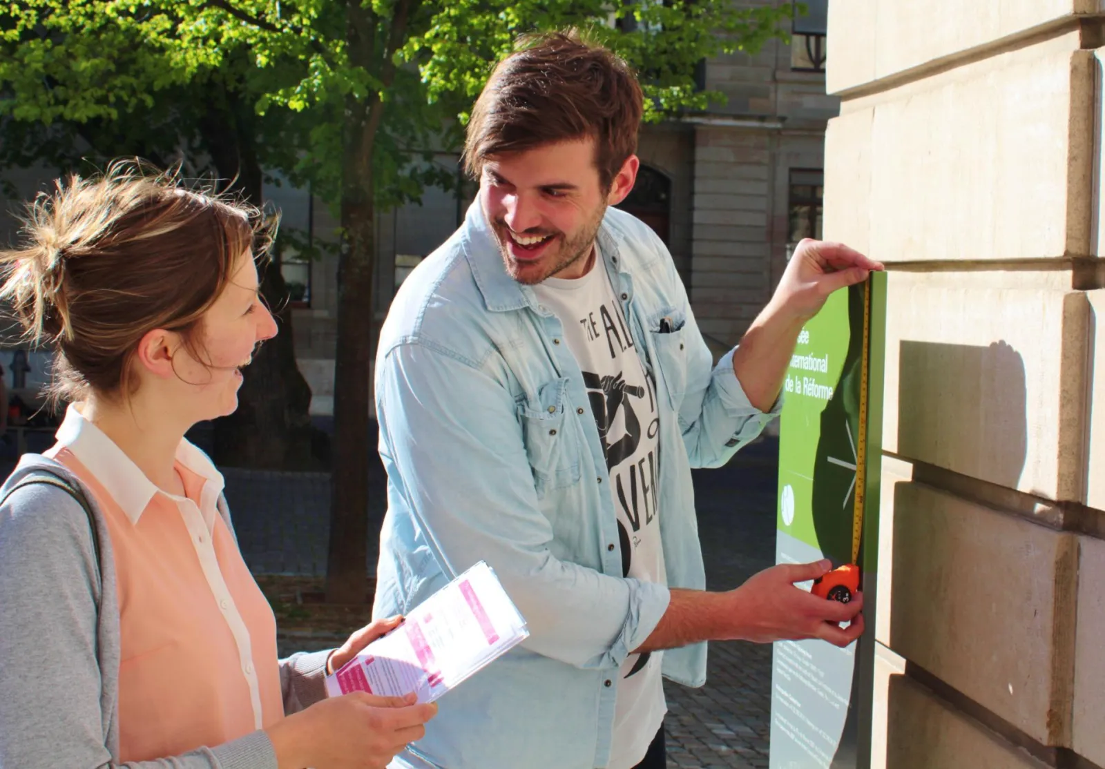 Two smiling young adults reviewing a document or map during an outdoor guided tour in Bordeaux, standing in front of a green information panel.