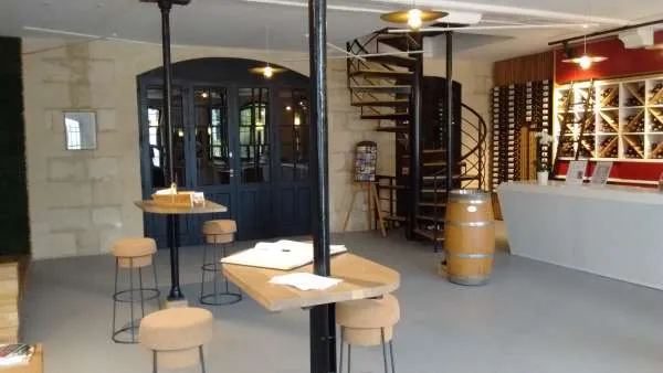 Modern interior of a wine cellar featuring a tasting counter, spiral staircase, oak barrels, and bottle displays at Château Lanessan in Bordeaux.