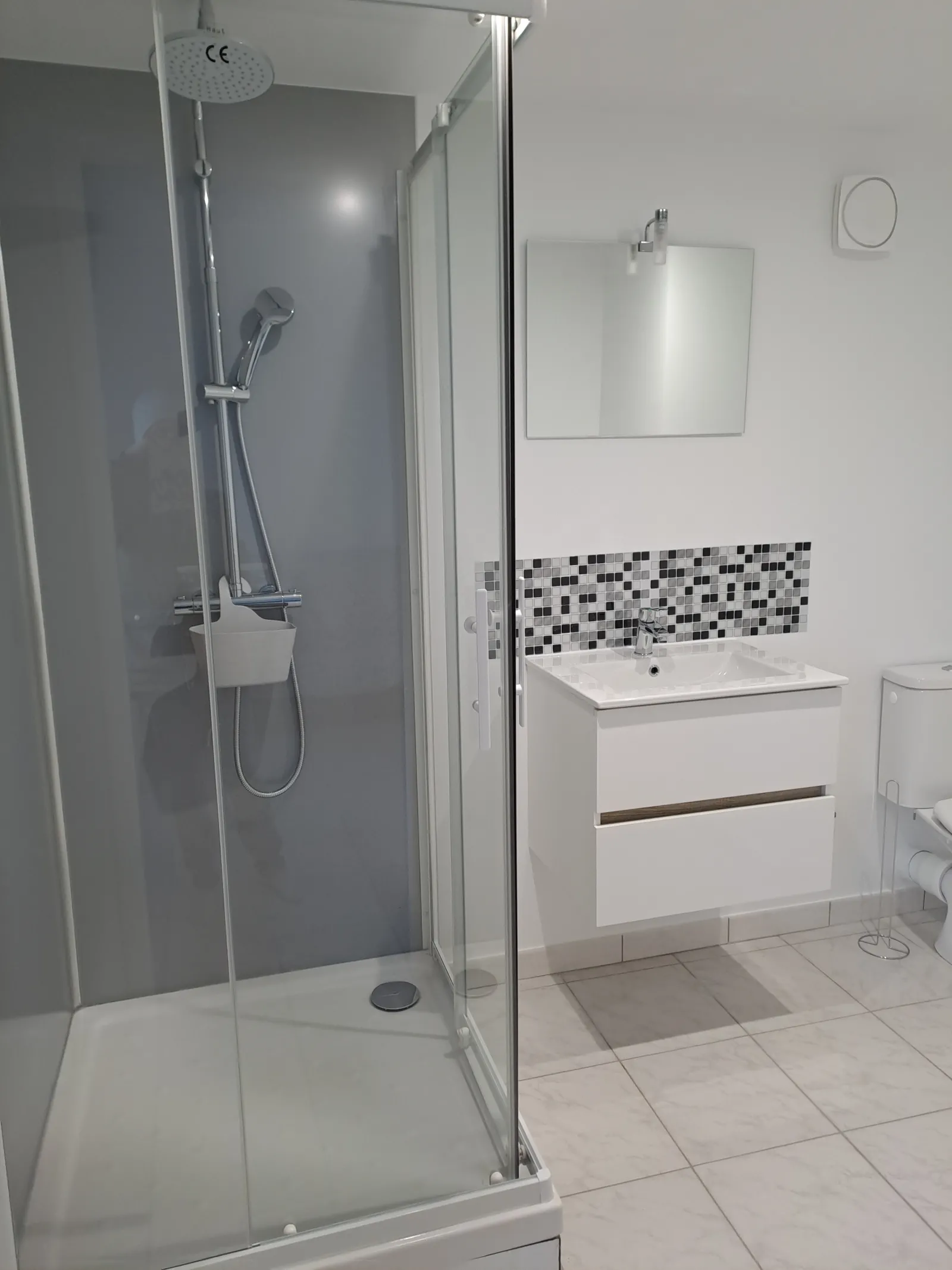 Modern bathroom with walk-in shower, white sink with mirror and black and white patterned tiles at the Anthocyane cottage of Château Pierre de Montignac in Bordeaux