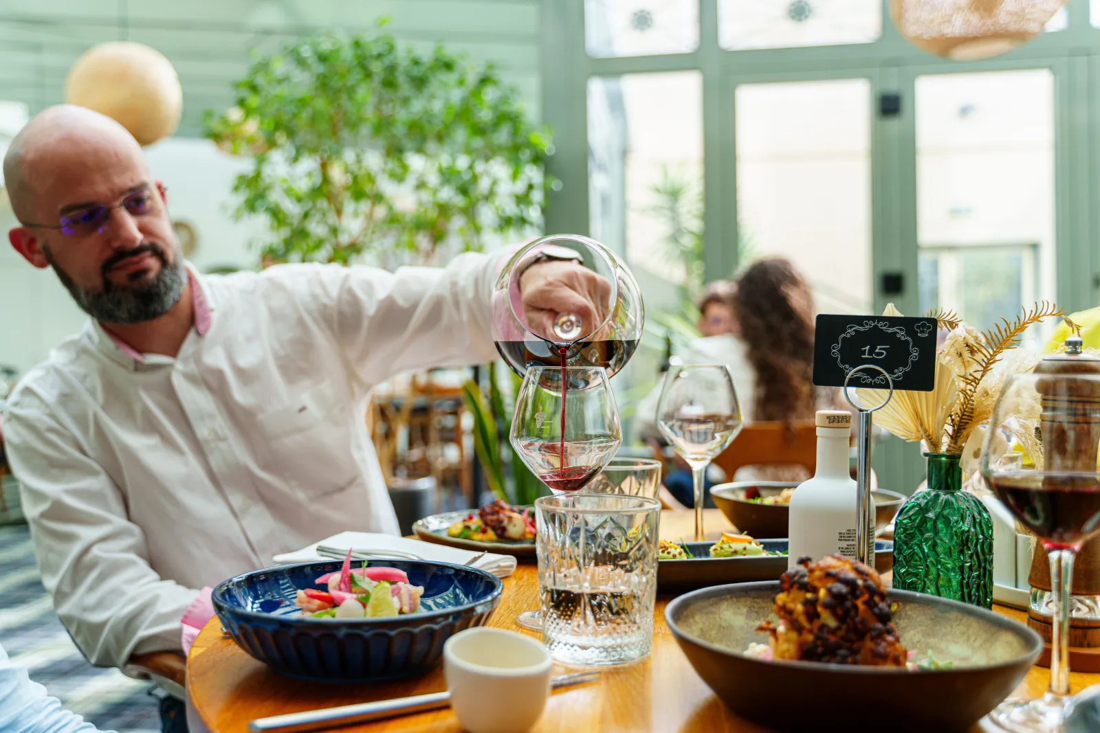 Chef pouring wine into a glass at an elegant fine dining table setup at C Restaurant in Bordeaux, with decorated plates and golden floral centerpieces