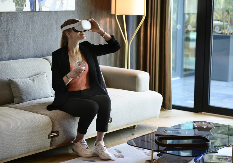 A woman in business attire sitting on a sofa uses a virtual reality headset in a modern and bright interior of Maison Cardinale in Bordeaux.