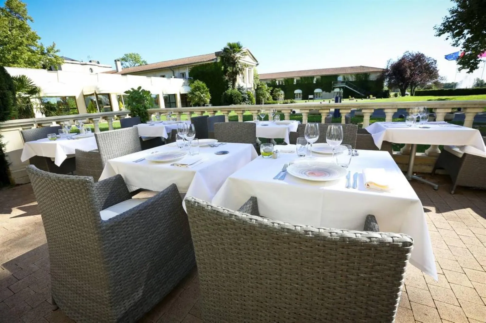 Elegant restaurant terrace with set tables, rattan chairs, white tablecloths and glassware, wine estate in the background near Bordeaux