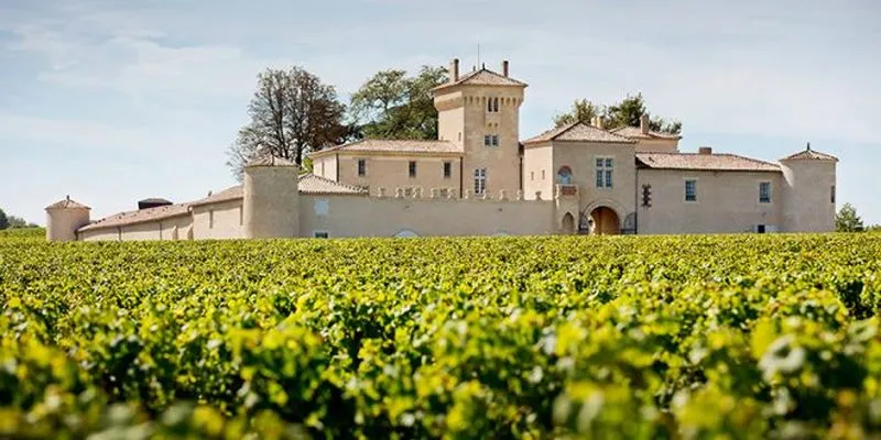 Château Lafaurie Peyraguey, an elegant stone castle with a square tower surrounded by lush vineyards in the Bordeaux wine region.
