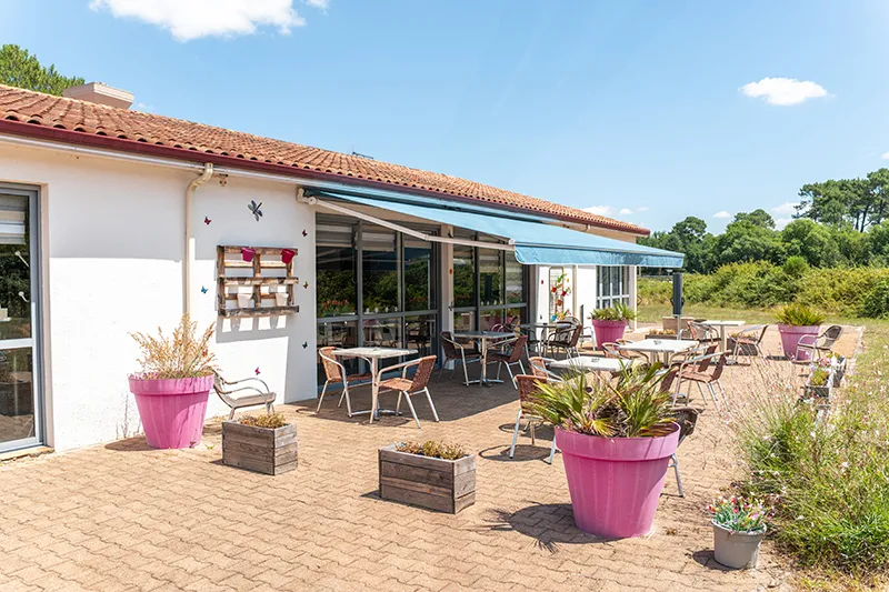Outdoor terrace of Kyriad Direct Bordeaux Sud Cestas hotel featuring garden furniture, pink flower pots, and white building with red tile roof