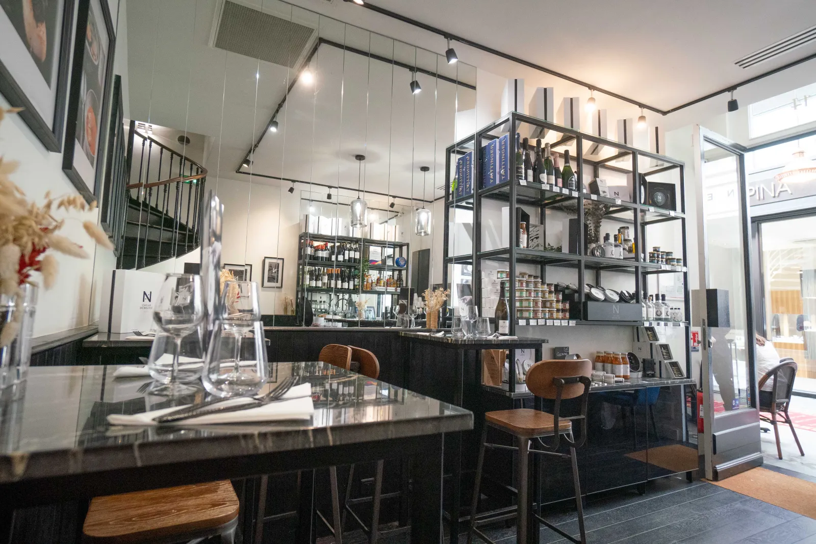 Modern and elegant interior of Caviar de Neuvic shop in Bordeaux, featuring a black counter, wooden stools, metal shelving displaying products, and pendant lighting.