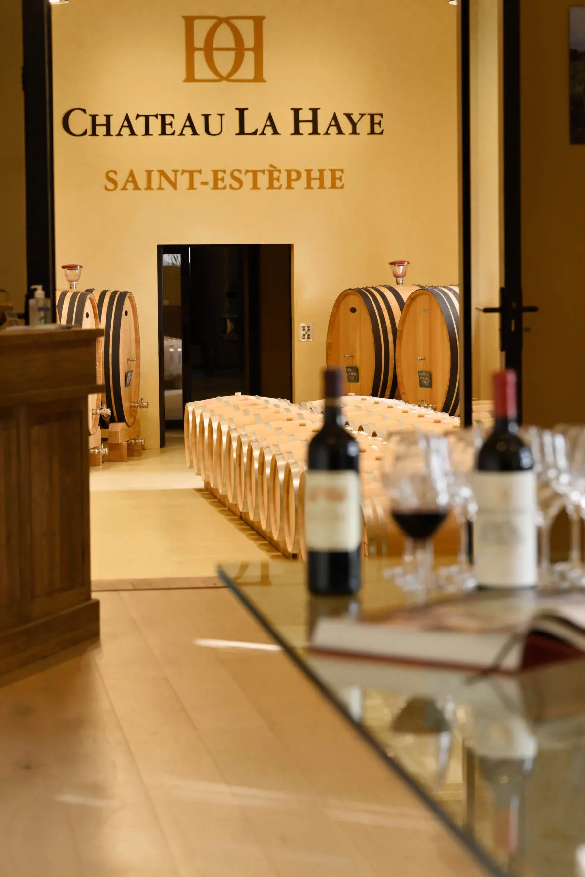 Interior of Château La Haye's wine cellar in Bordeaux, featuring oak barrels, tasting glasses and wine bottles in the foreground