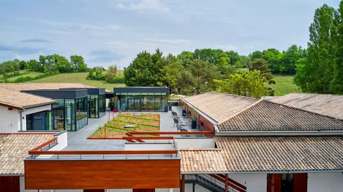 Aerial view of Maison Cardinale in Bordeaux, featuring modern architecture seamlessly integrated with historic buildings, clay tile roofs, green terraces, and landscaped outdoor spaces.