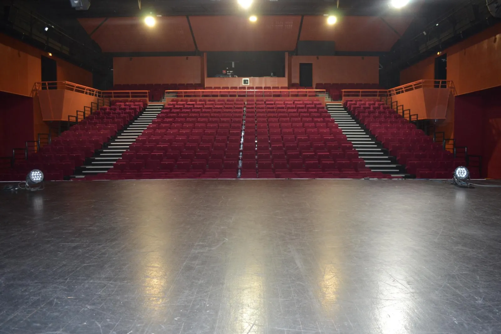 Interior of a modern cinema theater featuring red stadium-style seating, a black screen, orange walls, and a black ceiling with lighting fixtures.