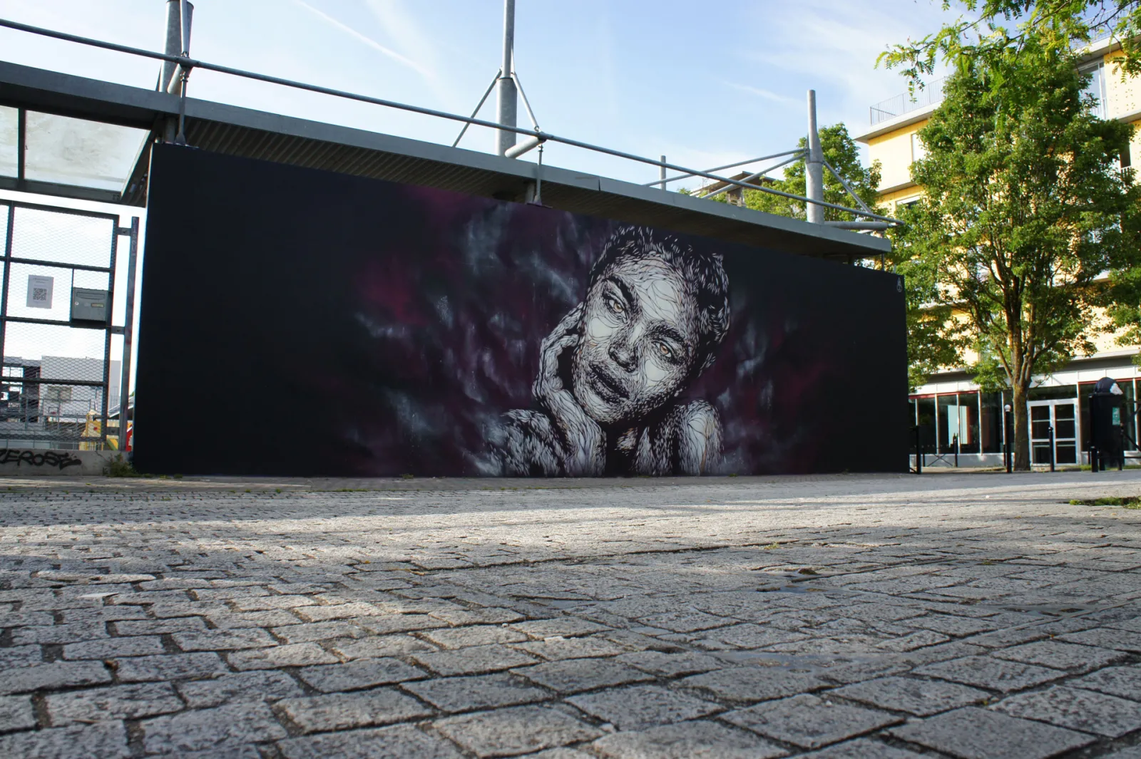 Black and white street art mural depicting an expressive portrait of a smiling woman painted on a large black wall in a public square in Bordeaux