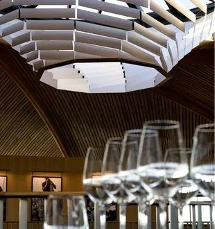 Interior of the Bordeaux Dome featuring a modern vaulted ceiling with natural light from an oculus, blurred wine glasses in the foreground, and dark wooden walls.