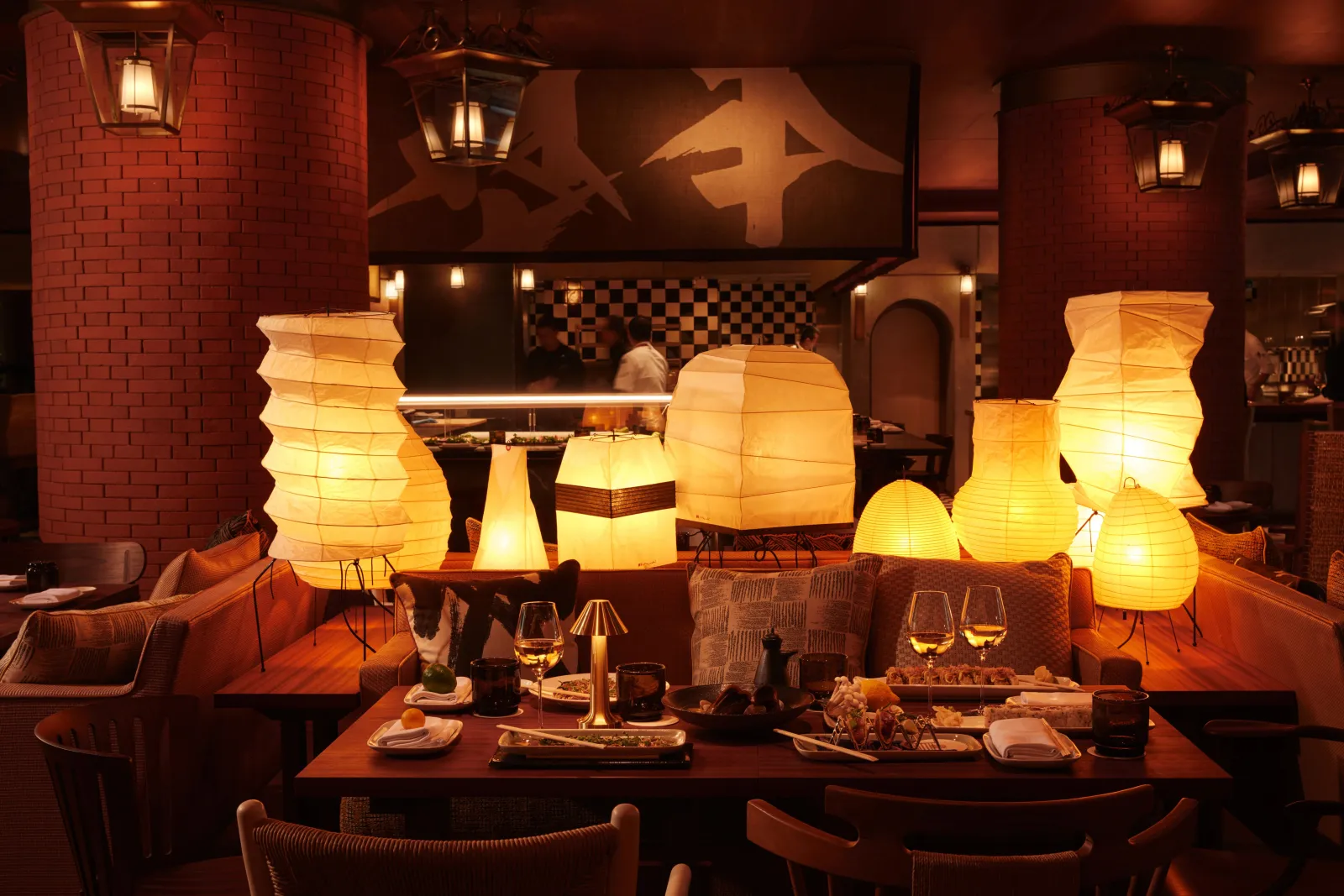 Elegant dining room at Mondrian Bordeaux Les Carmes featuring set tables, oversized illuminated Japanese lanterns, red brick walls, and modern warm-toned décor.