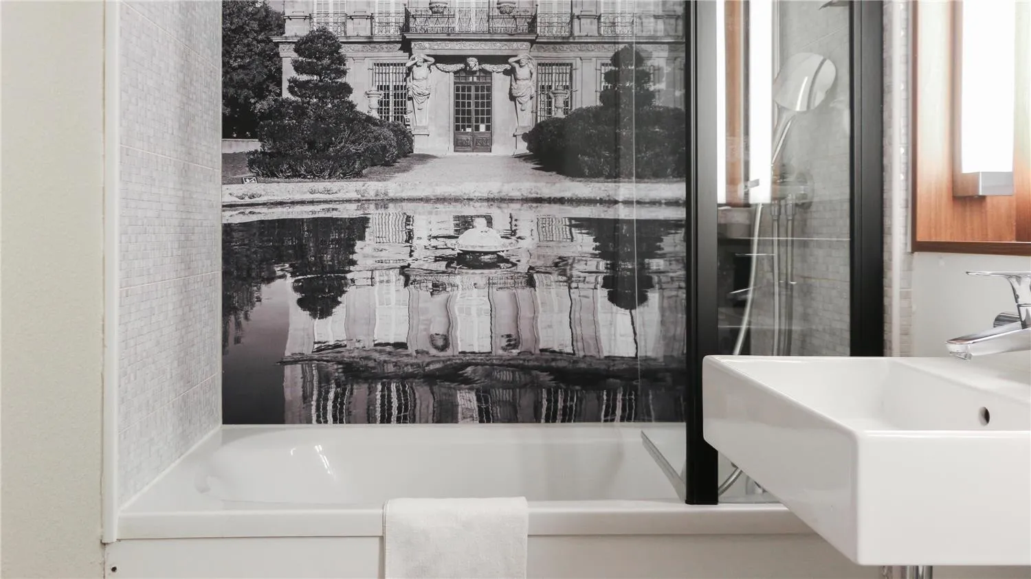 Modern bathroom with white bathtub and black and white photograph of a Parisian courtyard with reflecting pool, at Campanile Nature Bordeaux Lac