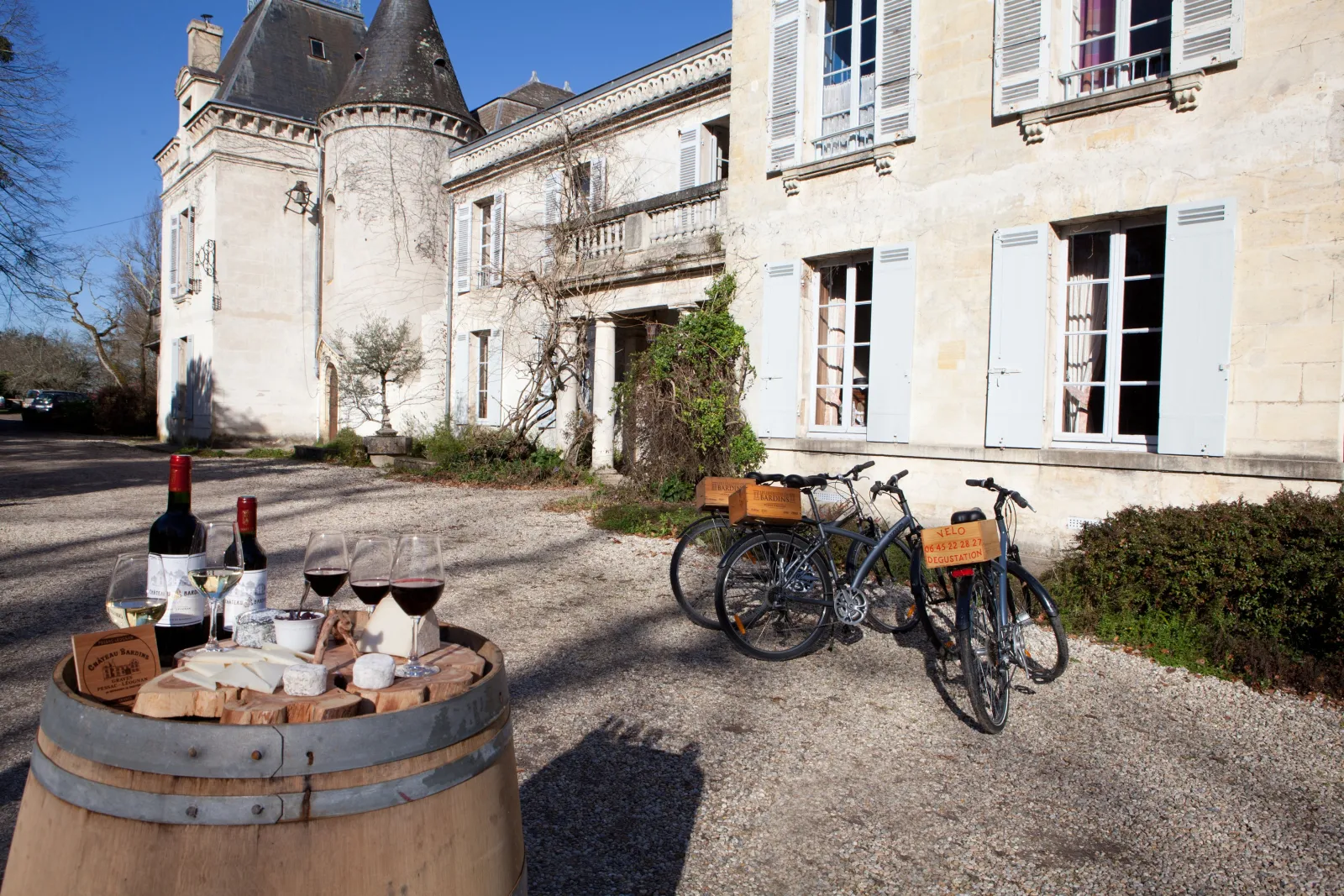 Wine and cheese tasting set on a wooden barrel in front of a castle courtyard with two bicycles parked nearby at Ateliers au Château in Bordeaux
