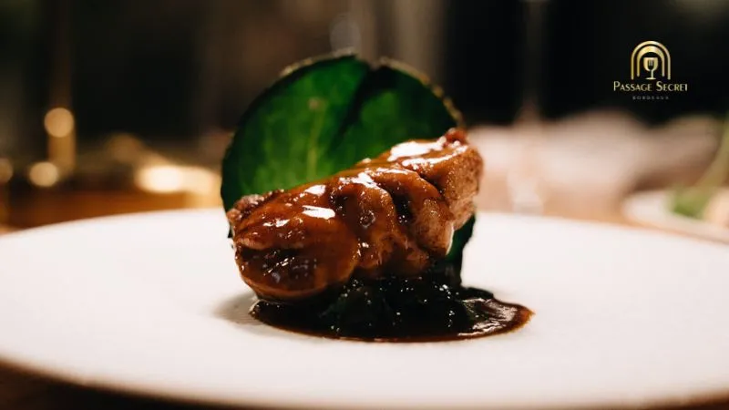 Gourmet dish from Passage Secret restaurant in Bordeaux: seared foie gras topped with fresh mint leaf on a dark sauce base, plated on white ceramic.