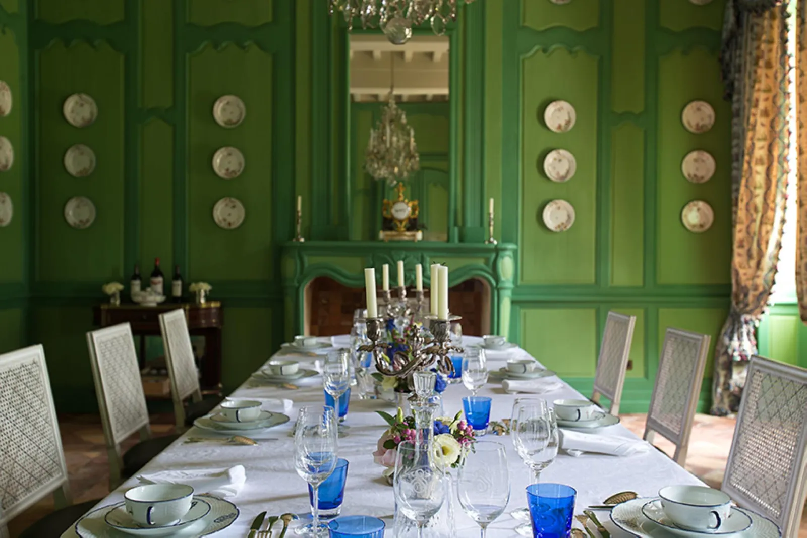 Elegant dining room at Château Soutard featuring emerald green walls, formally set table with place settings, gilt bronze candelabra, decorative plates and blue crystal glassware.