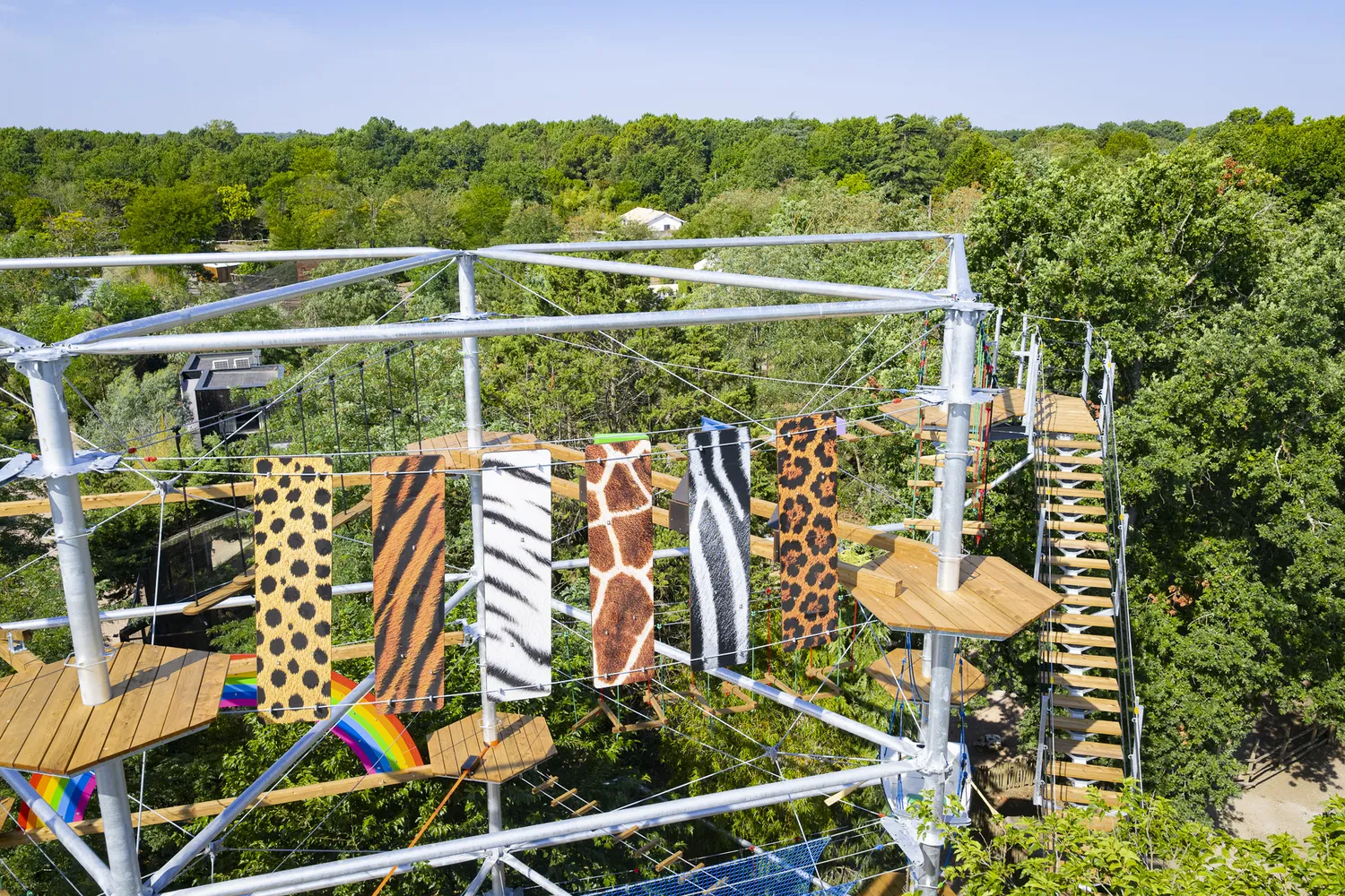 Aerial view of a platform with animal-patterned fabrics hanging on a metal structure, overlooking dense forest at Cimes de Bordeaux in Pessac.