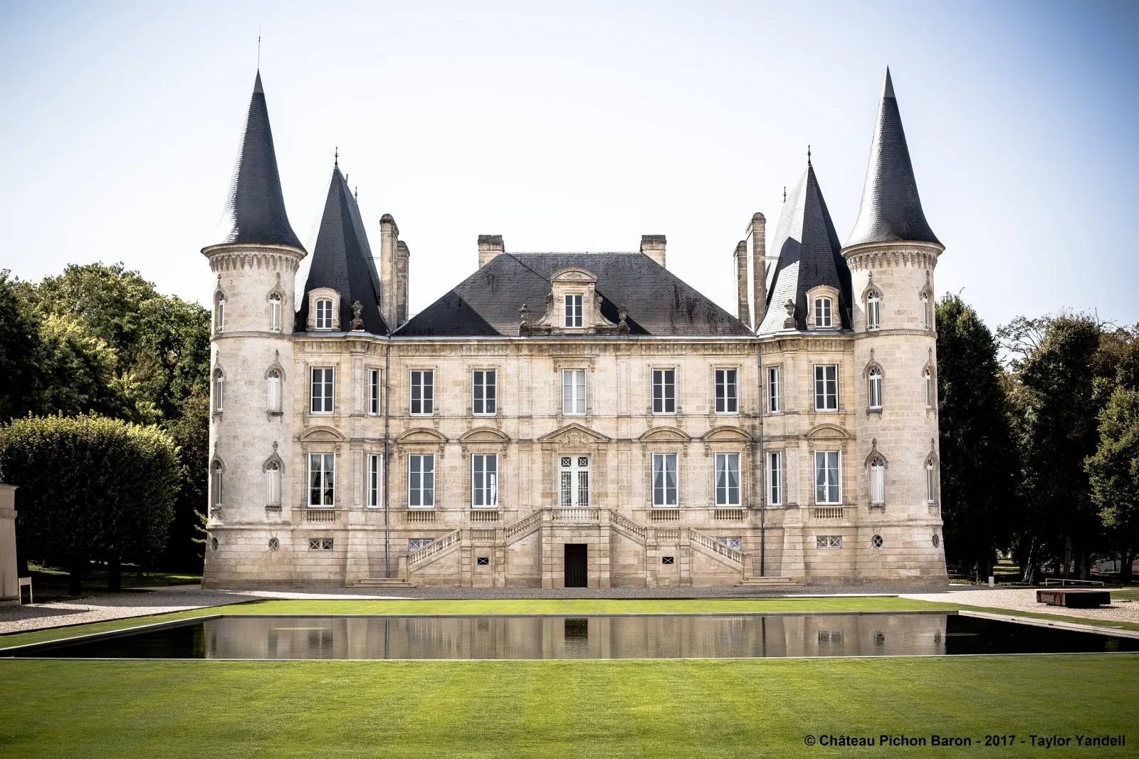 Château Pichon Baron in Bordeaux, a castle-style building with four pointed towers, light stone façade and reflection pool in the foreground